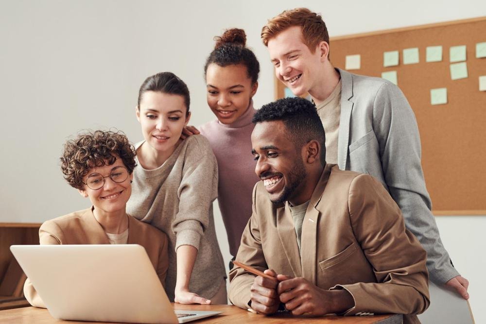 Smiling colleagues gathered around a laptop in an office